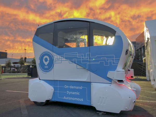 A self-driving pod photographed against a sunset background